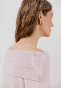 Svetřík bez ramínek v růžové barvě s žebrovaným výstřihem a jemnou texturou. Má uvolněný střih a jemné detaily kolem límce.
