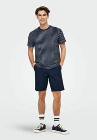 Chemise à rayures marines à manches courtes avec logo rouge, associée à un short marine et des chaussettes blanches à rayures noires, complétée par des baskets marines.
