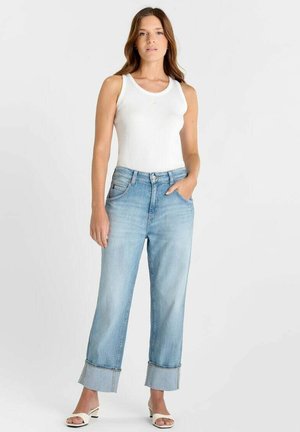 Lichtblauwe denim wijde broekspijpen jeans met opgerolde boorden, vijfzakkenontwerp en een taille die tot halverwege het middel reikt, gecombineerd met een wit nauwsluitend tanktopje.