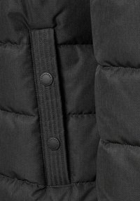 Detalje af sort dunjakke, der viser quiltet tekstur, et lodret panel med sorte knapper og en glat stoffinish.