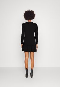 Black dress with long sleeves, a round neckline, and a ruffled hem. Made of soft material, it features fitted bodice details and a relaxed fit.