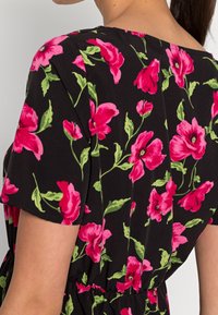 Robe noire à fleurs avec des fleurs roses vibrantes et des feuilles vertes, manches courtes et taille élastique pour une silhouette ajustée.