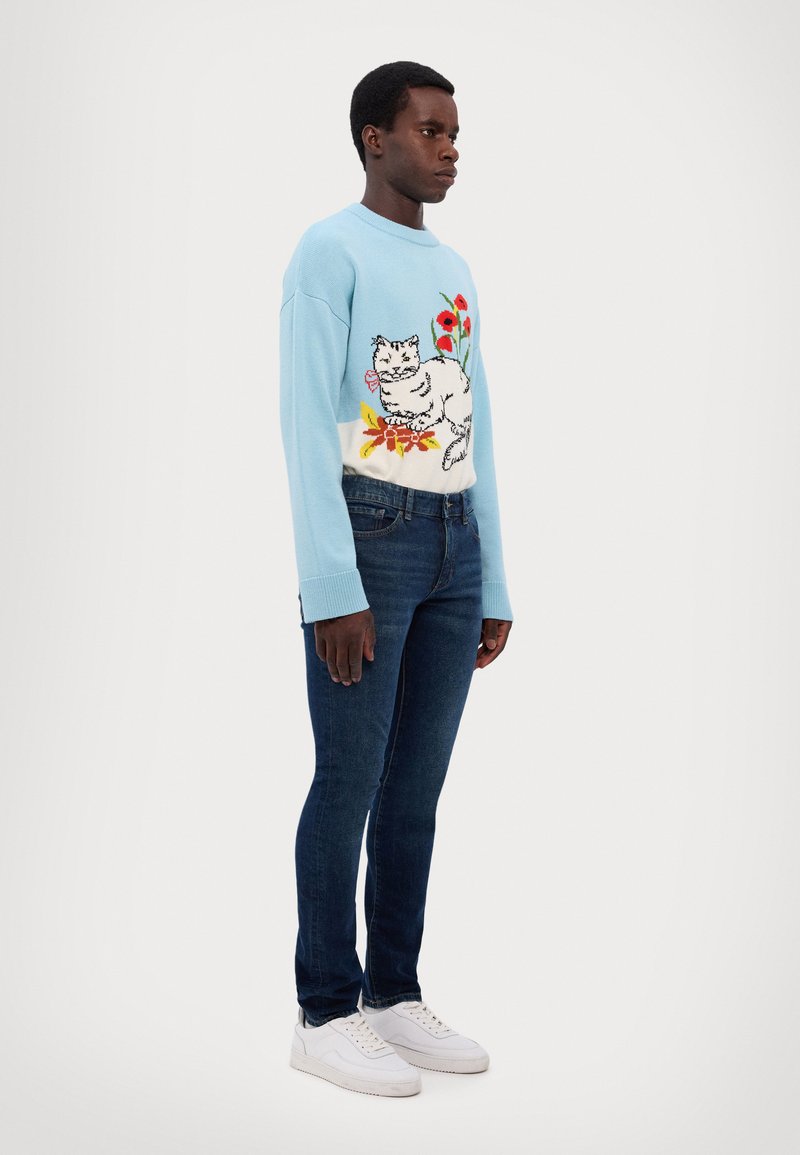 Light blue knitted sweater with cat and floral pattern; paired with dark blue jeans and white sneakers. Smooth texture, regular fit.