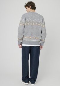 Pull en maille gris avec motifs géométriques en blanc et orange. Associé à un pantalon en denim bleu foncé ample et des baskets blanches.