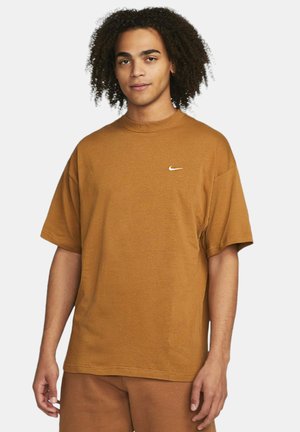 Brun bomulds T-shirt med rund hals og korte ærmer, der har et lille hvidt Nike-logo på brystet. Blød tekstur og afslappet pasform.