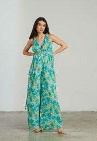 Robe maxi avec un motif floral vibrant en aqua et vert, dotée d'un décolleté en V profond, de bretelles halter et d'une taille cintrée avec une silhouette fluide.