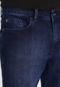 Dark blue denim jeans with a slim fit, featuring a front pocket, subtle whiskering, and classic five-pocket design. Smooth texture.