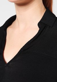Top nero a costine con collo e scollatura a V. Il tessuto ha una texture liscia con sottili linee verticali.