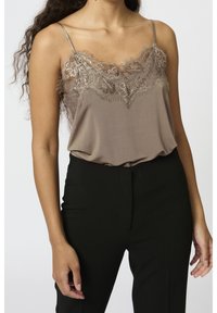 Ruskea toppi pitsireunuksilla, herkät hihnat ja sileä pinta, yhdistetty mustiin housuihin, esittäen kerroksellisia suunnitteluelementtejä.