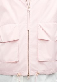 Ανοιχτό ροζ μπουφάν με κεντρικό φερμουάρ, δύο εμπρόσθιες τσέπες με καπάκι και ρυθμιζόμενα κορδόνια με χρυσούς στοπ στο τελείωμα.
