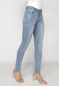 Jeans skinny azul claro con embellishments de lentejuelas en los bolsillos delanteros y detalles desgastados. Hechos de denim con una textura suave.