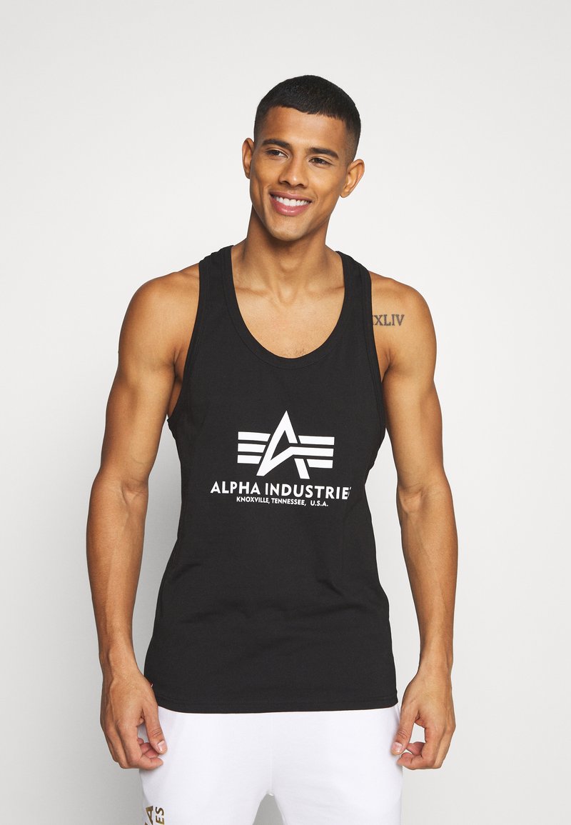 Schwarzes Tanktop mit einem großen weißen Logo, das "ALPHA INDUSTRIE" mit einem geometrischen Design zeigt. Der Stoff wirkt glatt und enganliegend.