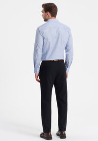 Jasnoniebieska koszula z guzikami w drobny wzór w kropki, zestawiona z czarnymi spodniami i brązowymi butami. Slim fit z długimi rękawami.