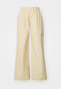 Wijdvallende, lichtbeige broeken met een elastische tailleband en een cargo pocket aan de zijkant. Gemaakt van zachte, gestructureerde stof.