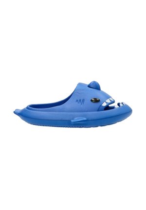 Zapatilla de goma con temática de tiburón azul, que presenta un diseño redondeado, detalles de cara depredadora y aletas salientes a los lados.
