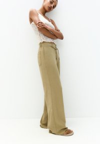 Beige wijde broek met een drawstring taille en zijzakken, gecombineerd met een kanten tanktop. Soepele stof en een relaxte pasvorm.
