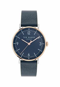 Ted Baker laikrodis su tamsiai mėlynu odiniu dirželiu, apvaliu tamsiai mėlynu ciferblatu, rožinės aukso rodyklėmis ir valandų žymekliais, turintis sidabrinį korpusą ir vainikėlį.