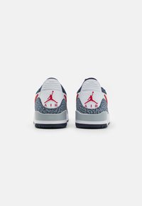 Kék és szürke sportcipők, a saroknál texturált elefántmintával, piros Jumpman logóval és fehér középső talppal. Hátsó nézet látható.