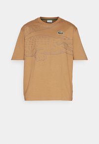 Brun bomull t-shirt med en krokodilgrafik i grått, korta ärmar, rak nederkant och en liten grön logotyp på bröstet.