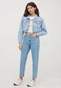 Giacca di jeans cropped azzurro chiaro con chiusura a bottoni e tasche, abbinata a jeans azzurro chiaro a vita alta e sneakers bianche. Finitura liscia.