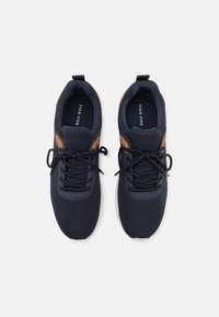 Baskets de sport bleu marine avec un dessus en tissu texturé, des accents en cuir marron, un bout rond et des lacets noirs, dotées d'une semelle intérieure rembourrée.