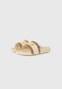 Beige liukuspontaskes, kurių juostos su leopardų raštu, su guminiais padais ir išsiskiriančiu geltonu logotipu ant viršutinių juostų.