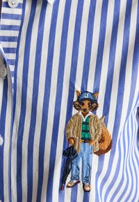 Striped blue and white shirt with embroidered fox wearing a hat, jacket, jeans, sneakers, and holding a folded umbrella.