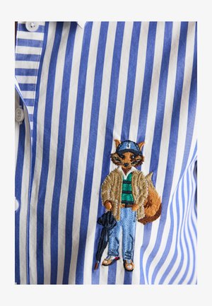 Striped blue and white shirt with embroidered fox wearing a hat, jacket, jeans, sneakers, and holding a folded umbrella.