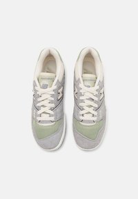Baskets grises et vertes en suède et mesh, avec une semelle intermédiaire crème, des lacets blancs et un logo "N" bien visible sur les côtés.