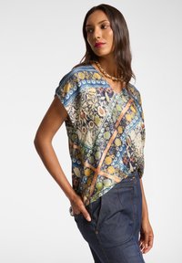 Blusa a maniche corte con un design vivace e stampato in blu, verde e giallo. Realizzata in tessuto leggero e morbido. Scollatura a V.