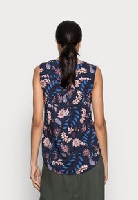 Blouse sans manches bleu marine avec un motif floral et de feuilles dans des tons roses et bleus, avec un ourlet arrondi et un tissu léger et doux.