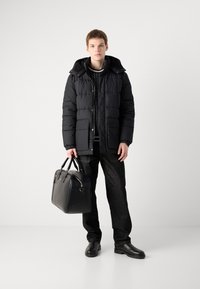 Black padded jacket with a hood, paired with a striped knit sweater and dark jeans, holding a black leather bag, finished with black shoes.