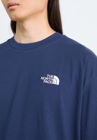 Navy blå bomulls t-skjorte med rund hals og korte ermer, med en hvit brodert logo på venstre bryst.