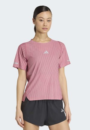 Młoda kobieta z ciemnymi włosami związanymi z tyłu, ubrana w różowy sportowy t-shirt w wzory i czarne szorty z białym logo na każdym z nich.