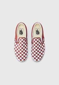 Paire de chaussures Vans enfilables avec un motif à damier marron et blanc et des semelles blanches sur un fond uni.