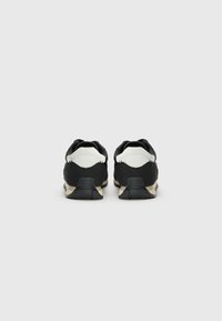 Black athletic shoes with white accents, textured fabric, and a sturdy black sole, featuring a low-cut design and padded collar.