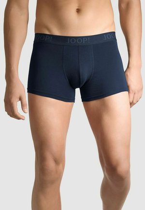 Pánský trup a nohy v tmavě modrých boxerkách s páskem s logem „JOOP!“ na neutrálním pozadí.