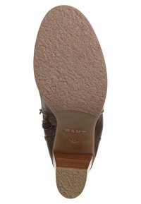 Botte cheville en cuir marron avec une semelle en caoutchouc texturée, fermeture éclair latérale et talon en bois clair marron. Présente une tige lisse et un bout arrondi.