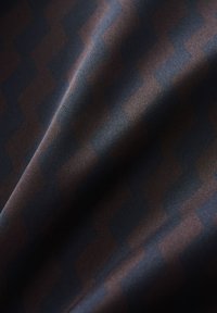 Stoff mit einem dunkelblauen und braunen Zickzackmuster, das eine glatte Textur und dezenten Glanz zeigt. Klassisches geometrisches Design auf weichem Material.
