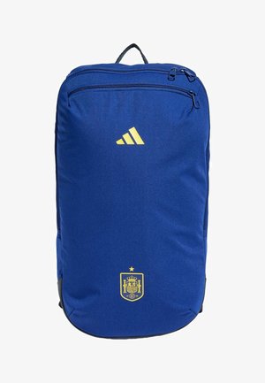Mochila azul hecha de tela duradera, con un logo amarillo de Adidas, un escudo español y dos compartimentos con cremallera.