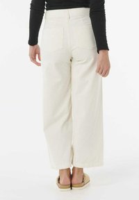Viddebenet, ribbestrikkede hvide bukser med høj talje, to baglommer og en afslappet pasform. Sammen med beige slip-on sko.