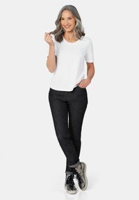 Weißes kurzärmeliges T-Shirt kombiniert mit dunkelblauen Jeans. Die Jeans haben einen umgeschlagenen Saum, und glänzende silberne Turnschuhe runden das Outfit ab.