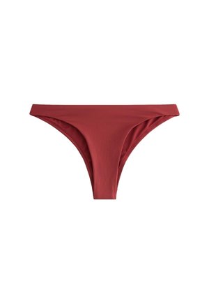 Kobieta stoi przy basenie w bordowych majtkach od bikini i dopasowanym staniku bikini z metalową klamrą z tyłu.