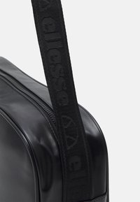 Czarna syntetyczna torba na ramię z teksturowanym wykończeniem, wyraźnym zamkiem błyskawicznym oraz plecionym paskiem z detalami logo. Kompaktowy i prostokątny kształt.