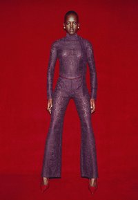 Lace bodysuit in deep purple with a turtleneck and flared pants. Features intricate floral patterns. Paired with red high-heel shoes.