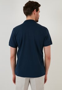 Tmavě modré polo tričko s krátkým rukávem, vyrobené z texturované látky a s skládacím límcem. Design zahrnuje klasický střih a rovný lem.