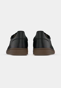 Μαύρα συνθετικά αθλητικά παπούτσια με υφή, με καφέ ελαστική σόλα και τρεις μαύρες ρίγες στα πλά�για.