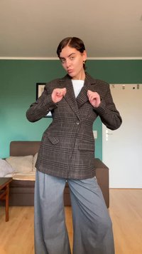 Plaid blazer in brown and black, featuring a notched lapel, two front pockets, and a single button closure, paired with wide gray pants.