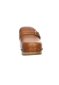 Sabot en cuir marron avec un bout arrondi, des clous métalliques décoratifs le long de la semelle, des coutures blanches et une bride à boucle en laiton sur le dessus.