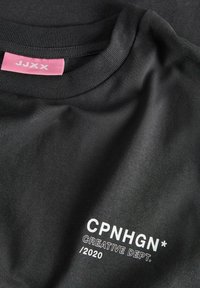Sort bomulds t-shirt med rund halsudskæring, prydet med hvid trykt tekst "CPNHGN* CREATIVE DEPT. /2020" og et pink label ved halsen.